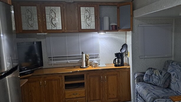 A compact kitchen with wooden cabinets, a refrigerator, a coffee maker, and a microwave.