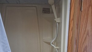 A bathroom with a shower, a wooden door, and a white towel hanging on the wall.