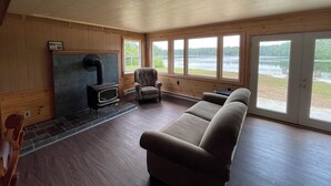 A cozy cabin interior with a stone fireplace, a sofa, and large windows overlooking a lake.