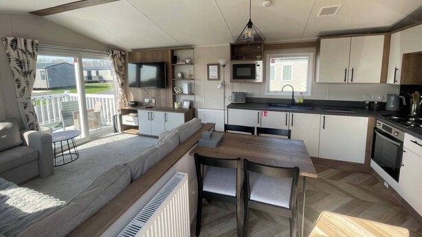 A modern kitchen with a dining area, a built-in TV, and a large window overlooking a yard. - 3-bed Caravan - Haven Lakeland Leisure Park (Grange-over-Sands)
