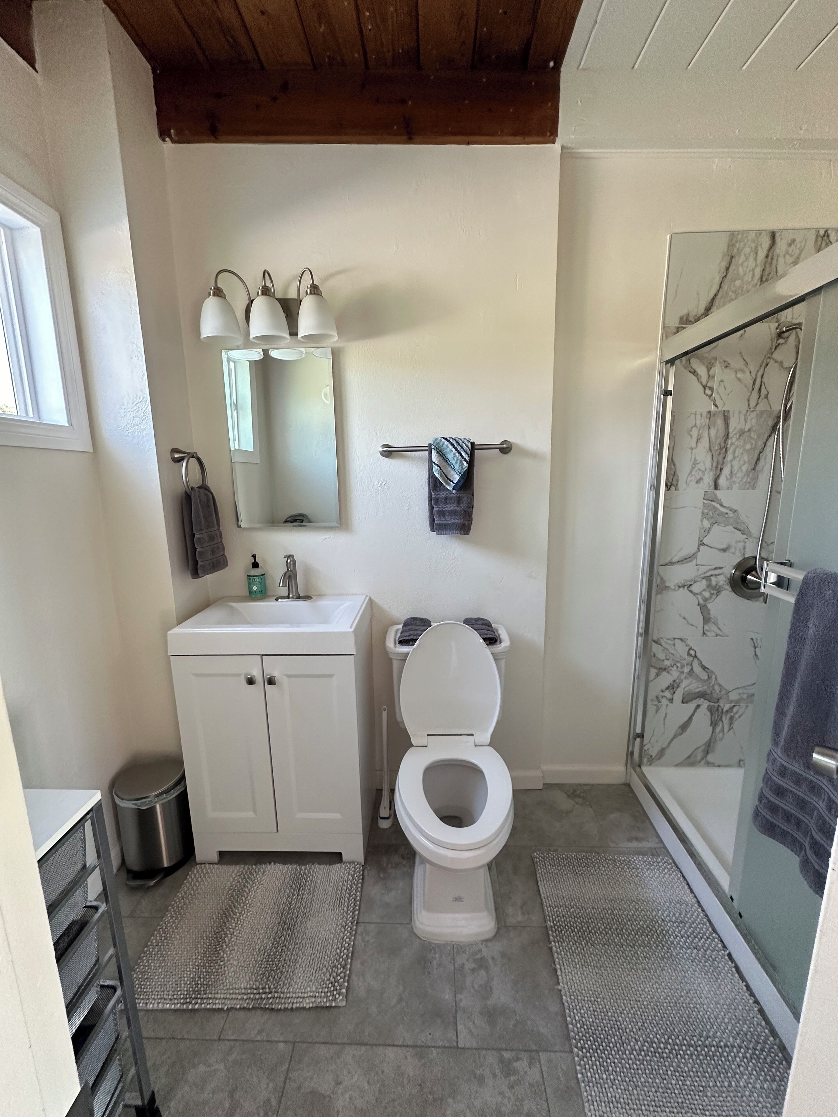 A bathroom with a white toilet, a sink, a mirror, and a shower with marble tiles.