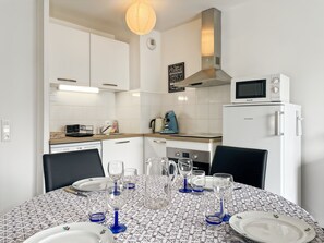 A modern kitchen with white cabinets, a microwave, a coffee maker, and a dining table set for four. - Le Réséda, Maison Avec Jardin (Saint-Valery-sur-Somme)
