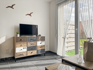 Una sala de estar moderna con televisor de pantalla plana, un mueble de madera con cajones y un ventanal corredero a un jardín.