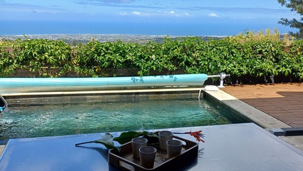 Ein Tisch am Pool mit einer Tablett voller Gläser und einer Flasche, mit Blick auf den Pool und die Aussicht auf Meer und Grünflächen.