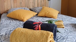Ein ordentlich bezogenes Bett mit gemusterten Bettwaren, zwei gelbe Kissen und einem hölzernen Kopfteil.