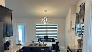 A modern kitchen with dark cabinetry, a central island, a stainless steel oven, and a marble floor.