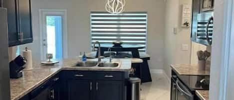 A modern kitchen with dark cabinetry, a central island, a stainless steel oven, and a marble floor.
