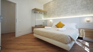 A modern bedroom with a large bed, a bedside table, a mirror, and a wall-mounted light fixture.