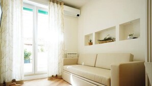 A room with a beige sofa, a window with curtains, and wall-mounted shelves with plants.