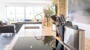 A modern kitchen with a central island, a built-in stove, and a knife block. - The Duchess - North East Escapes (Bamburgh)