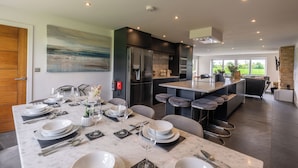 A modern kitchen with a marble countertop, stainless steel appliances, and a dining area set for a meal. - The Duchess - North East Escapes (Bamburgh)