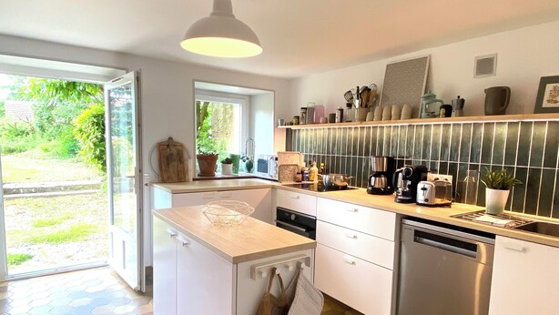 Una cucina moderna con isola centrale, mobili bianchi, lavastoviglie e un'ampia finestra che offre luce naturale.