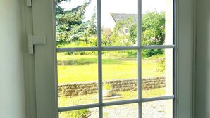 Una porta bianca con una finestra a griglia, che mostra un giardino con un muro in pietra, una pianta in vaso e una casa sullo sfondo.