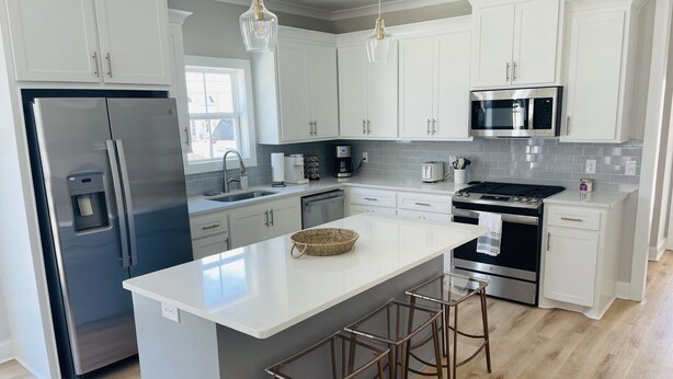 A modern kitchen with white cabinets, stainless steel appliances, a central island with stools, and pendant lighting.