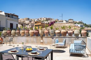 Zona pranzo all'aperto con un tavolo imbandito per due persone, circondato da sedie e con vista su vasi in terracotta e edifici sullo sfondo.