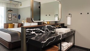 Una habitación de hotel moderna con una cama, un espejo grande, un tocador de mármol y un baño con inodoro y lavabo.