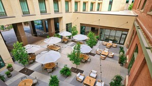Terraza en la azotea con mesas y sillas, rodeada de plantas en macetas y sombrillas.