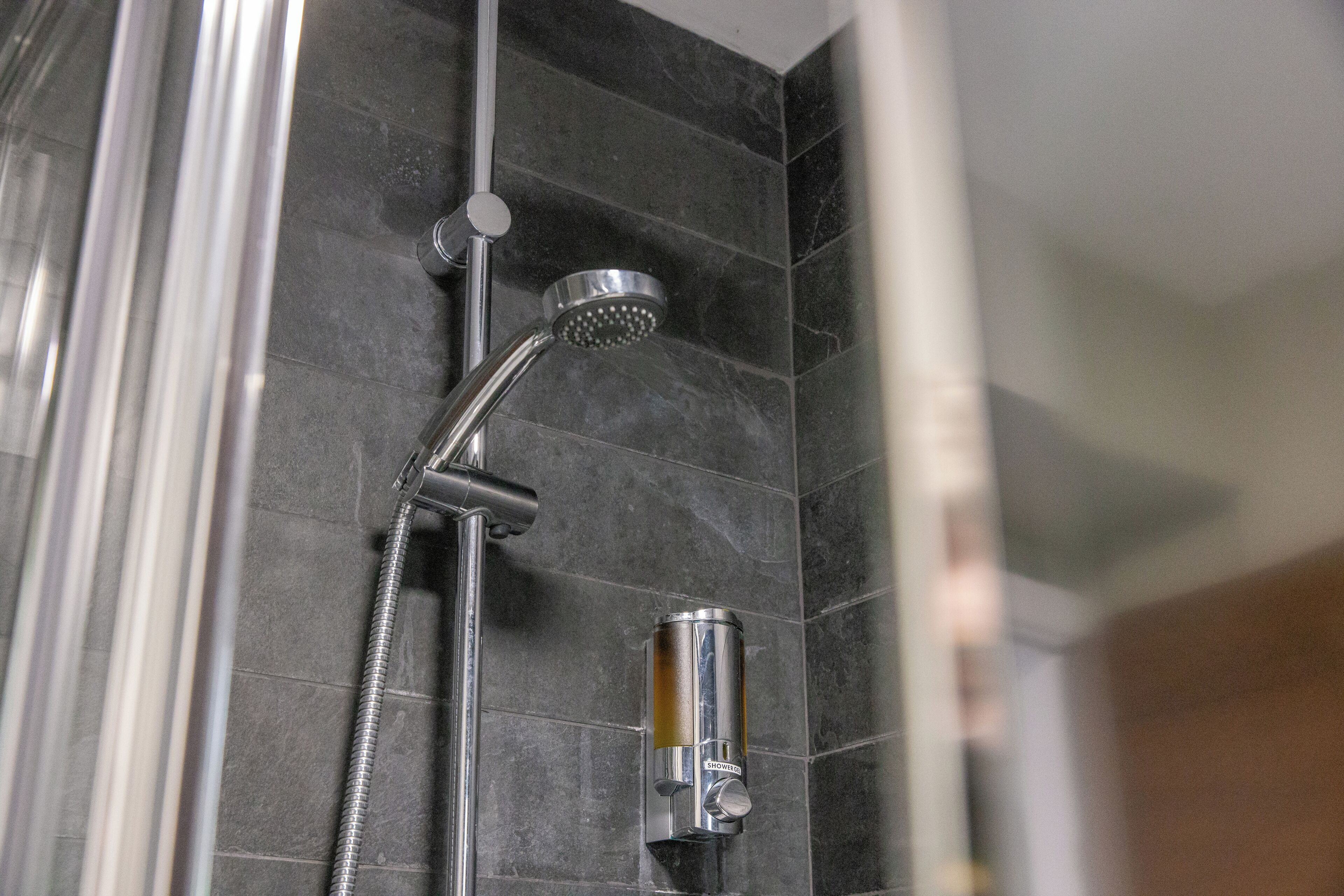 Une douche équipée d’un pommeau de douche à main et d’un panneau de commande fixé au mur.