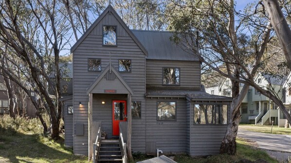 Stunning two-story building with a steeply pitched roof and symmetrical facade, featuring a red door and charming entrance.