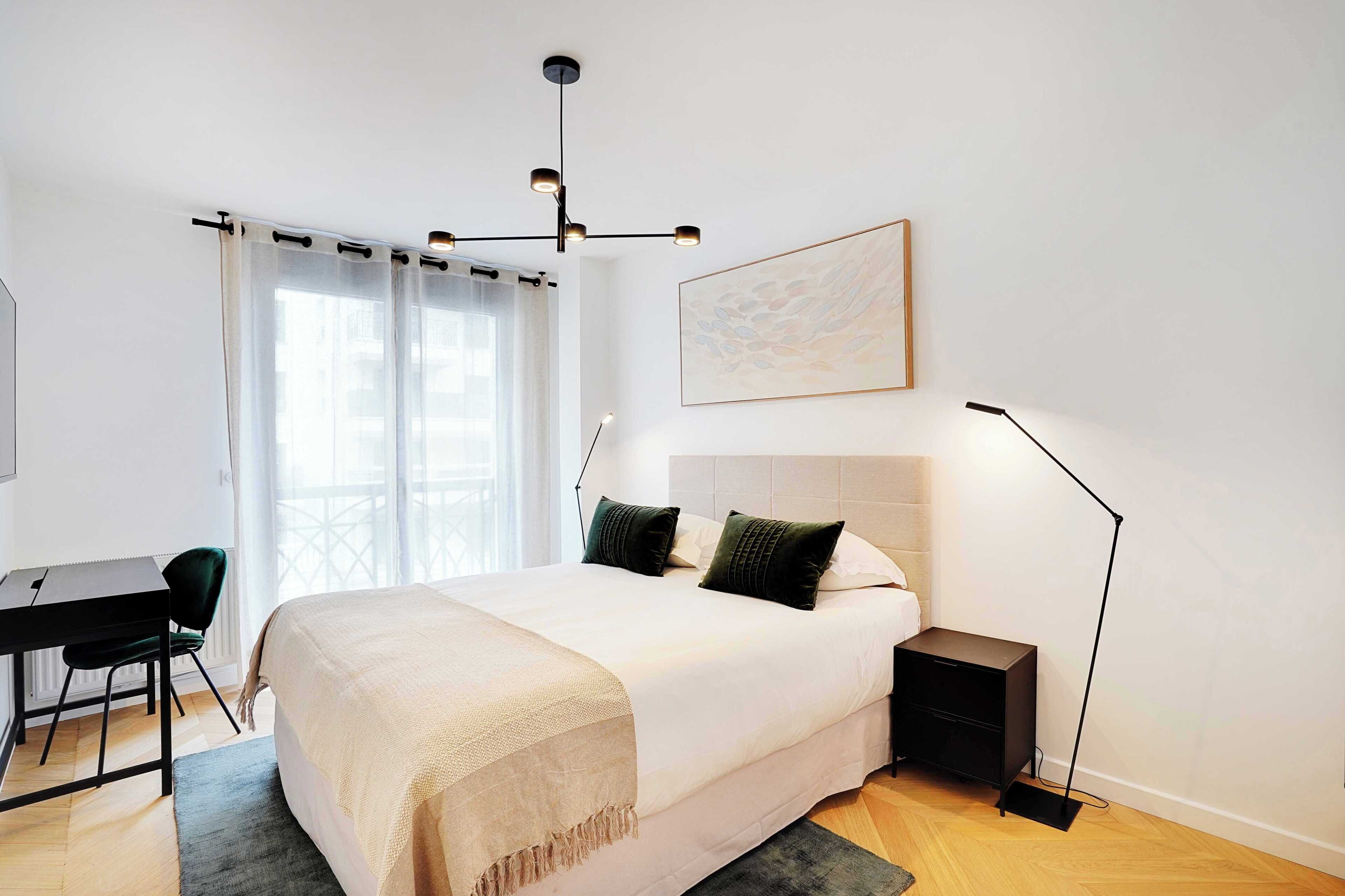 Una camera da letto con un letto, un comodino, una scrivania, una sedia e una lampada da terra.