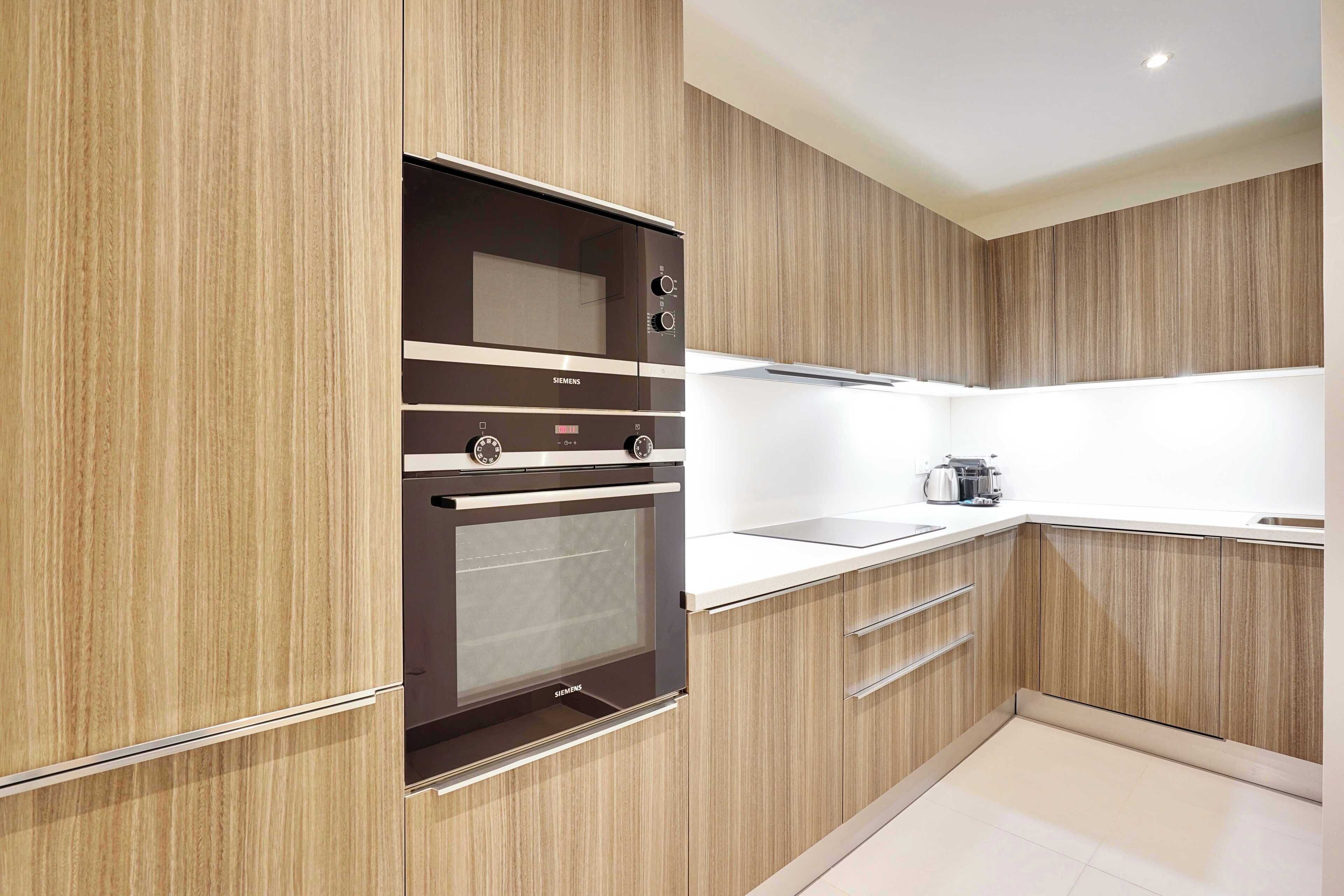 A modern kitchen with wooden cabinetry, a built-in oven, and a stainless steel range hood.
