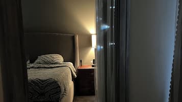 Ein schmaler Flur führt zu einem Schlafzimmer mit Bett, Nachttisch und Lampe.