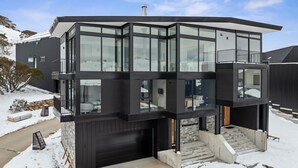 Et moderne hus med to etager, store glasvinduer, en garage og en trappe op til øverste niveau.