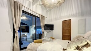 Un dormitori amb llit, cortines, una porta de fusta i vista a un balcó.