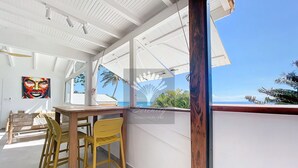 Una habitació amb una taula i cadires de fusta, un finestral gran que mostra el mar, i un sostre amb bigues blanques.