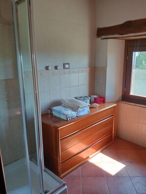 Une salle de bain avec un meuble-lavabo en bois, une cabine de douche en verre et une fenêtre laissant entrer la lumière naturelle.