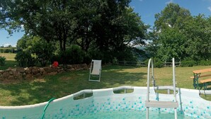 Ein Schwimmbecken mit Fliesen umgeben von einer Rasenfläche mit Bäumen und einer Steinmauer.