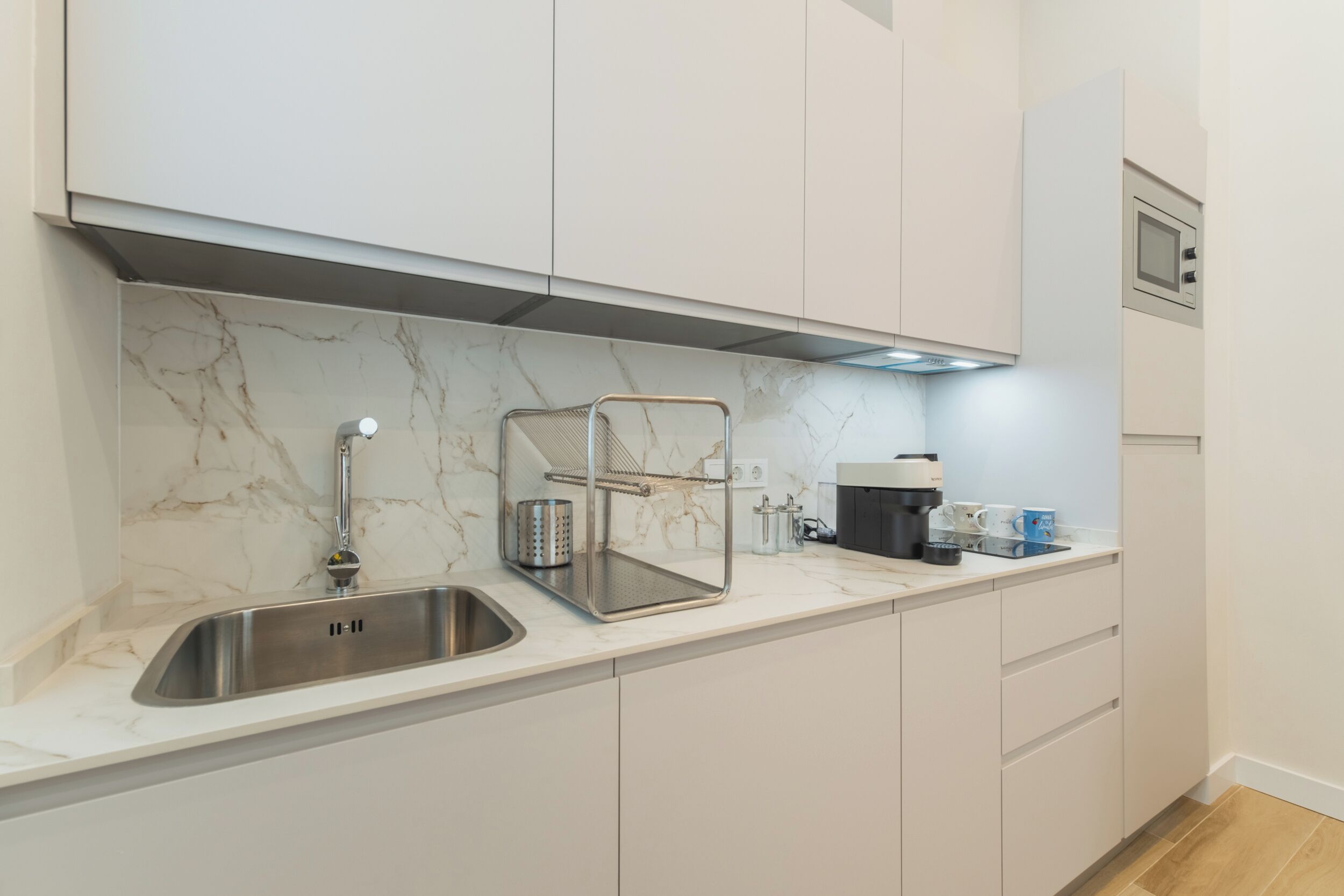 A modern kitchen with a marble backsplash, stainless steel sink, and white cabinetry.