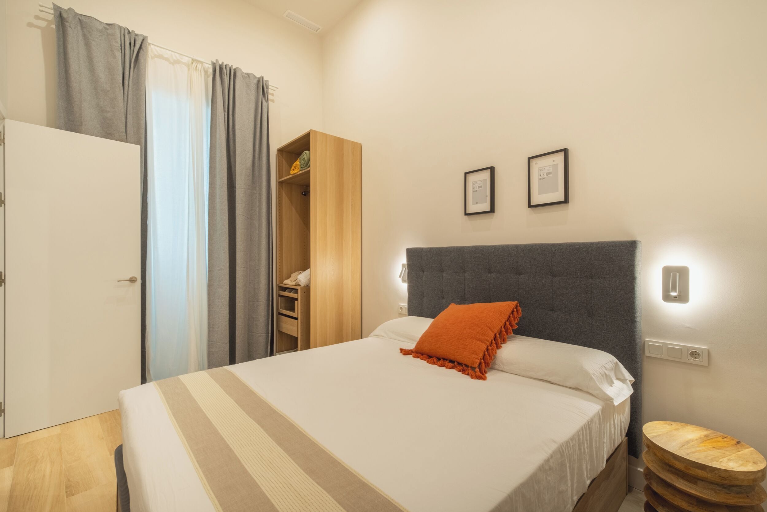 Un dormitorio con cama, armario, mesita de noche y un taburete de madera.