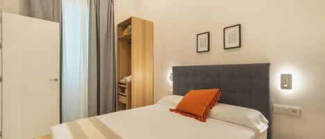 Un dormitorio con cama, armario, mesita de noche y un taburete de madera.