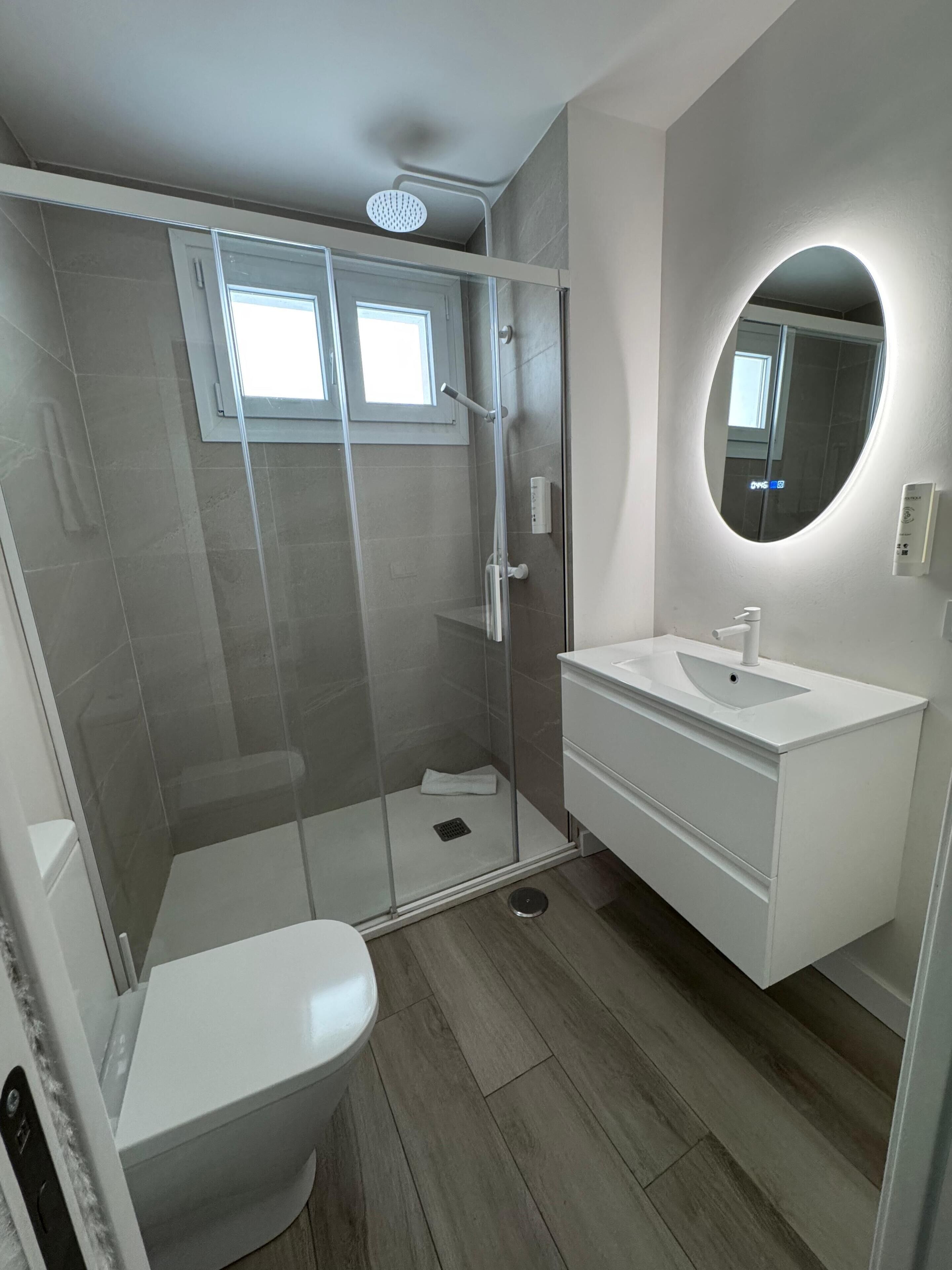 Une salle de bain moderne avec une douche à parois de verre, un lavabo blanc et un miroir rond.