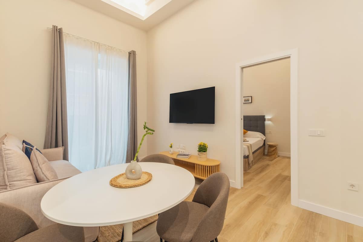Un salon moderne avec une table ronde blanche, un canapé gris et un téléviseur fixé au mur.