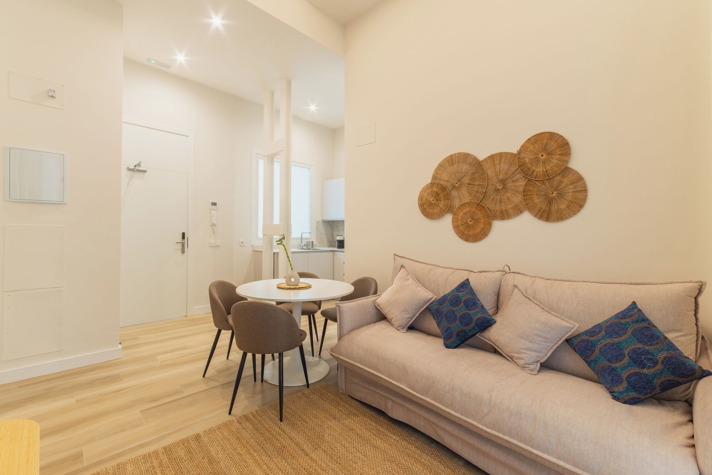 Una sala de estar moderna con un sofá color beige, cojines estampados, una mesa de centro redonda y un adorno en la pared.