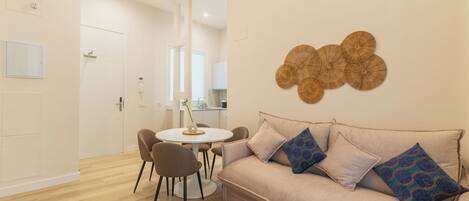 A modern living room with a beige sofa, patterned cushions, a round coffee table, and a wall-mounted decorative piece.
