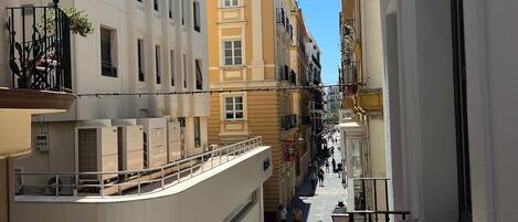 Una estrecha calle urbana flanqueada por edificios, un cielo azul despejado y algunos peatones.