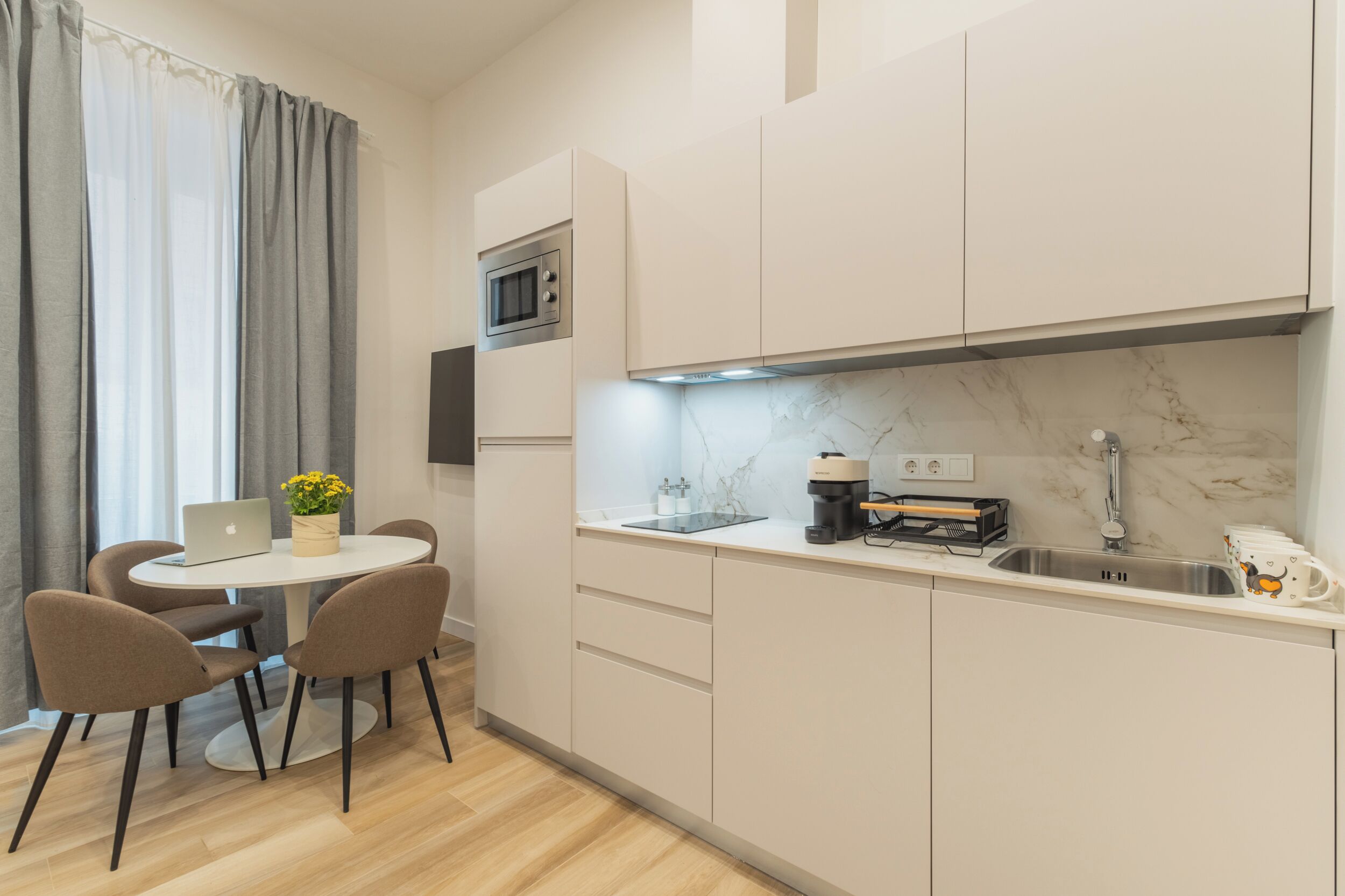 A modern kitchen with a round dining table, chairs, a built-in oven, and a marble backsplash.
