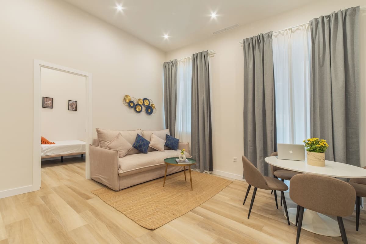 Un salon moderne avec un canapé, une petite table, une table à manger avec des chaises et un ordinateur portable posé sur la table à manger.