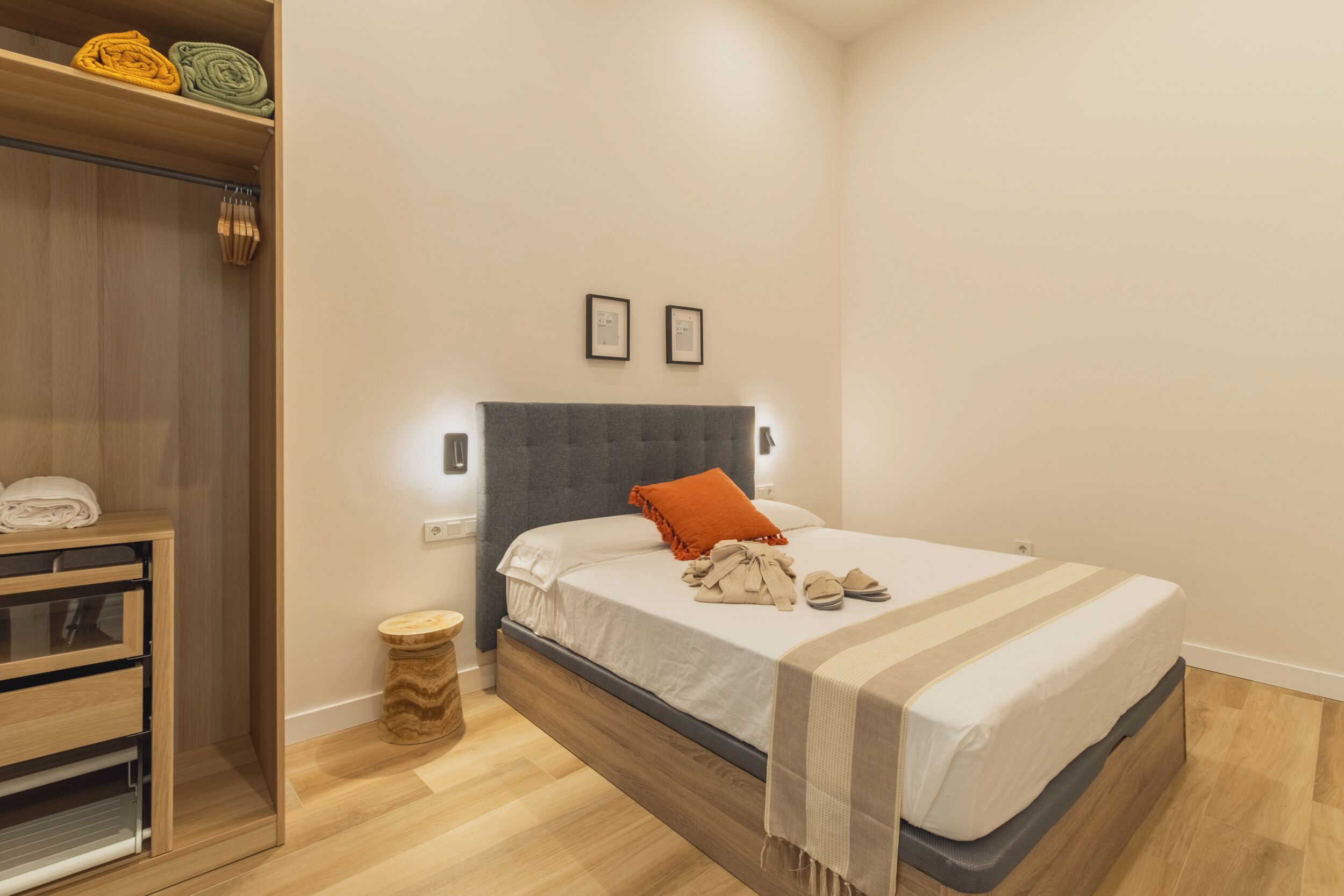 A neatly arranged bedroom with a bed, bedside tables, a wardrobe, and a small round wooden stool.