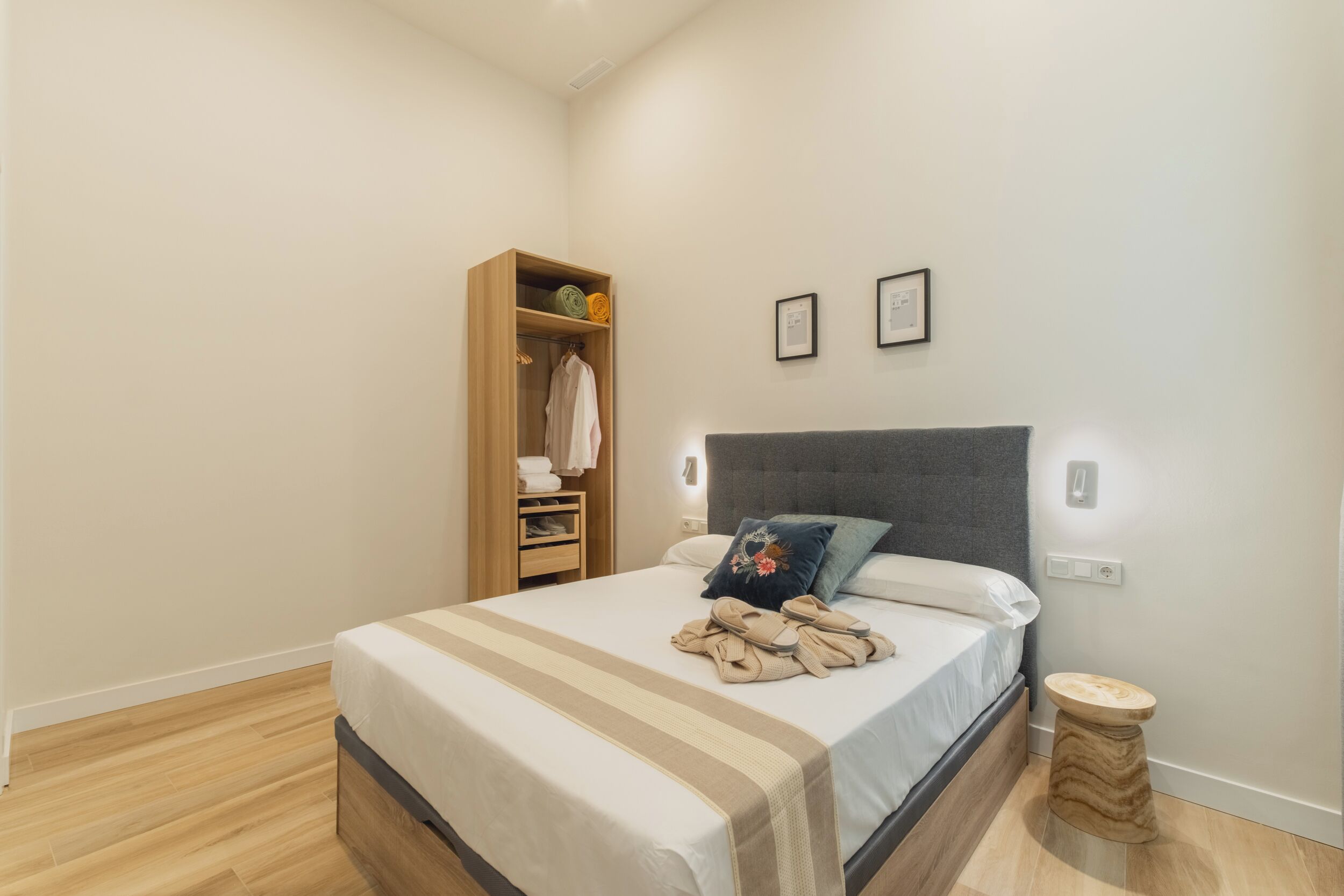 A neatly arranged bedroom with a bed, a wooden wardrobe, and a small round stool.