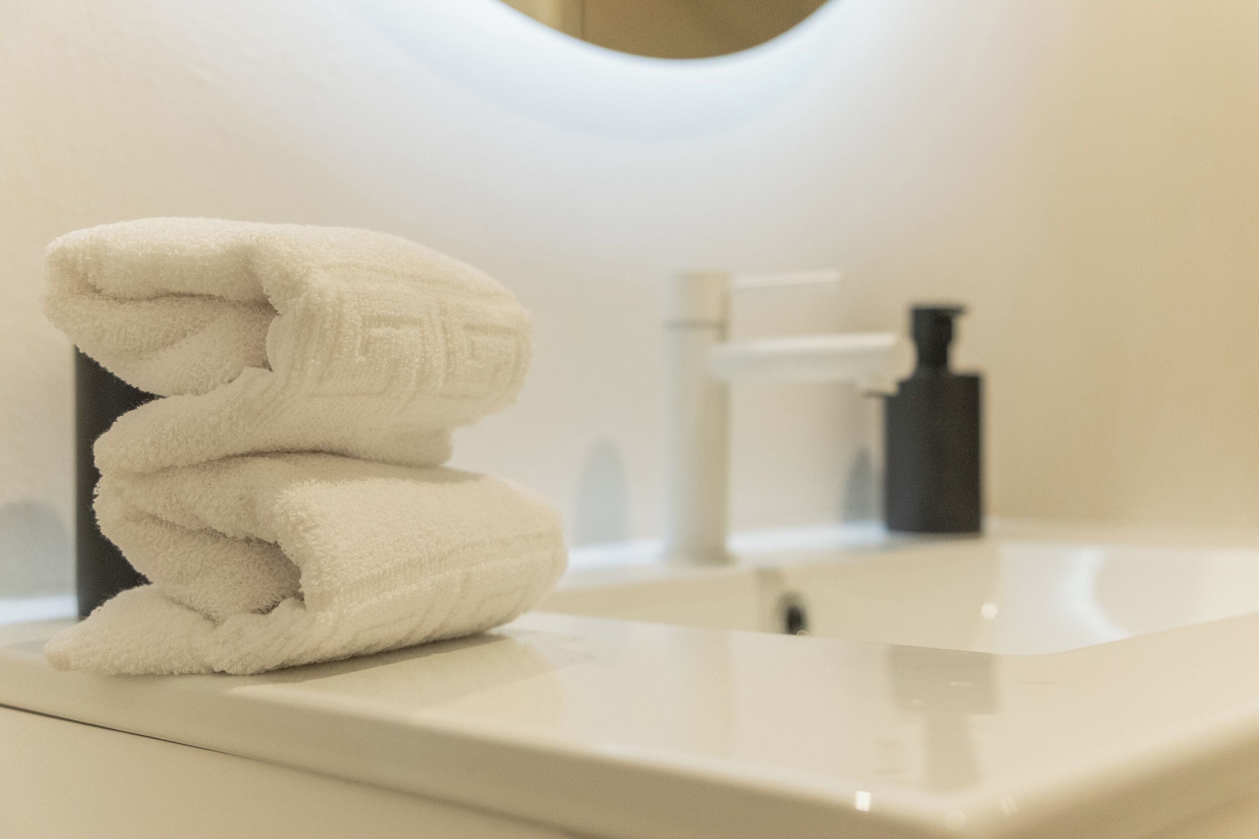 A bathroom with a white sink, a towel stacked on the edge, and a bottle of soap.
