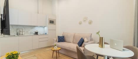 A modern living room with a sofa, coffee table, and a dining area with a laptop and vase.