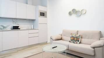 Una sala de estar moderna con un sofá, una mesita redonda y una cocina con alacenas blancas y un microondas.
