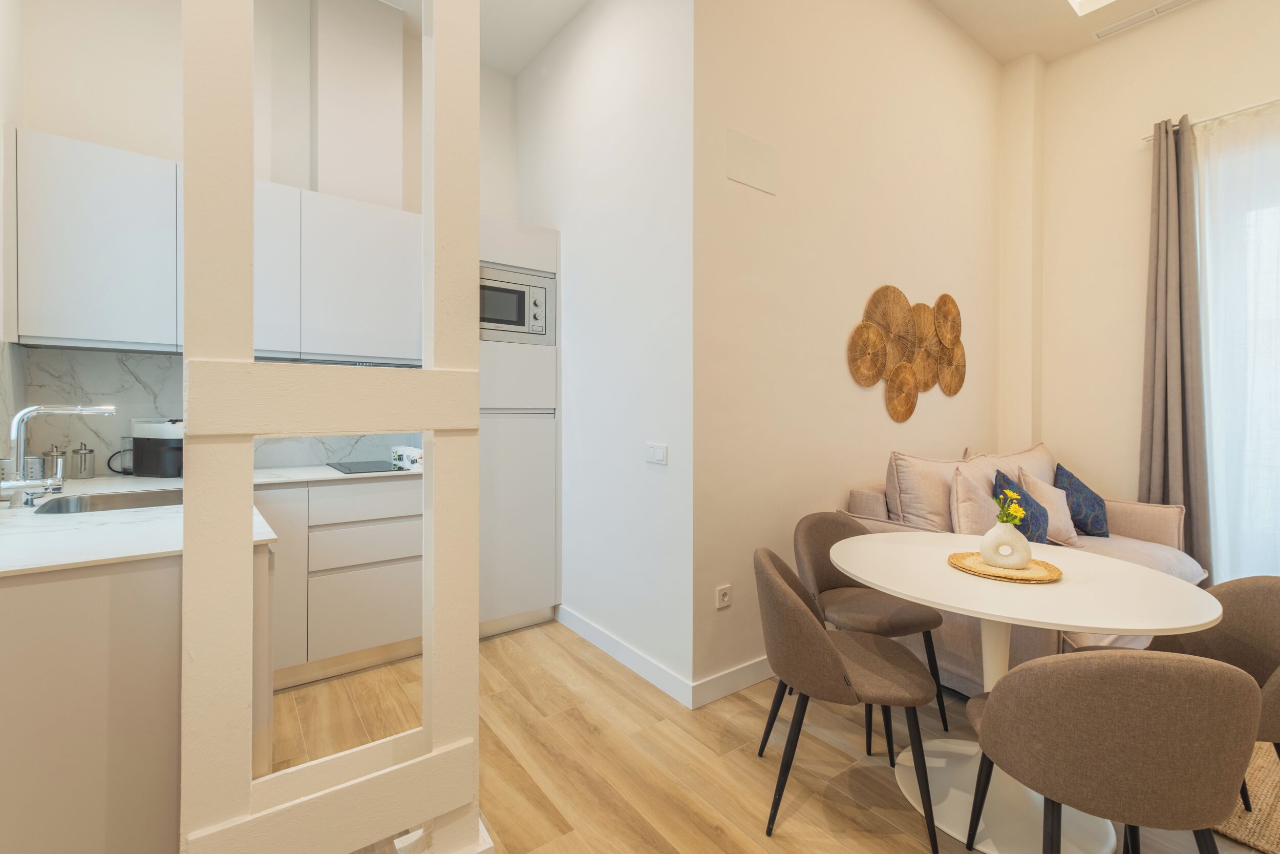 A modern kitchen with white cabinets, a microwave, and a sink. There is a dining area with a round table and four chairs.