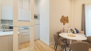 A modern kitchen with white cabinets, a microwave, and a sink. There is a dining area with a round table and four chairs.
