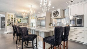 A modern kitchen with a large island, bar stools, a chandelier, and stainless steel appliances. - SPEND YOUR SPRING BREAK IN A HOT TUB/HEATED POOL on the ISLAND! (Galveston)