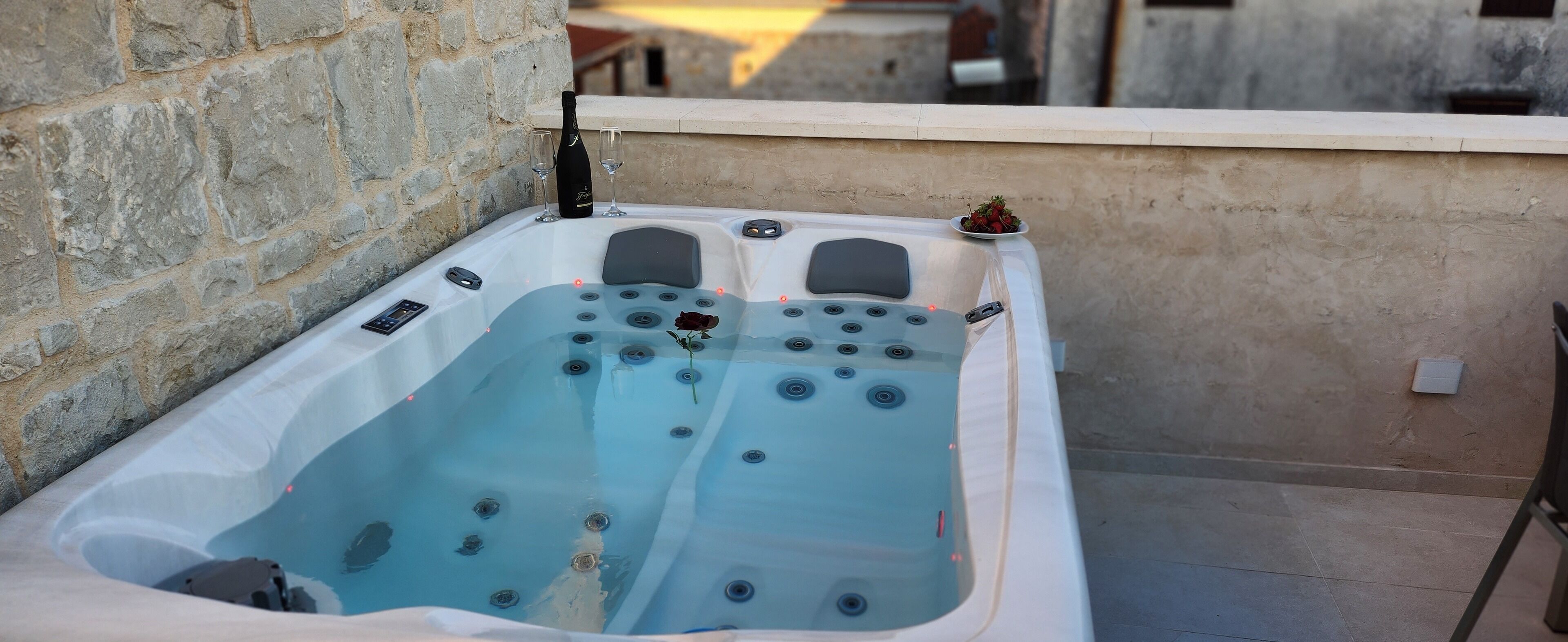 A hot tub with multiple jets, a rose, and a bottle of champagne on a balcony with stone walls.
